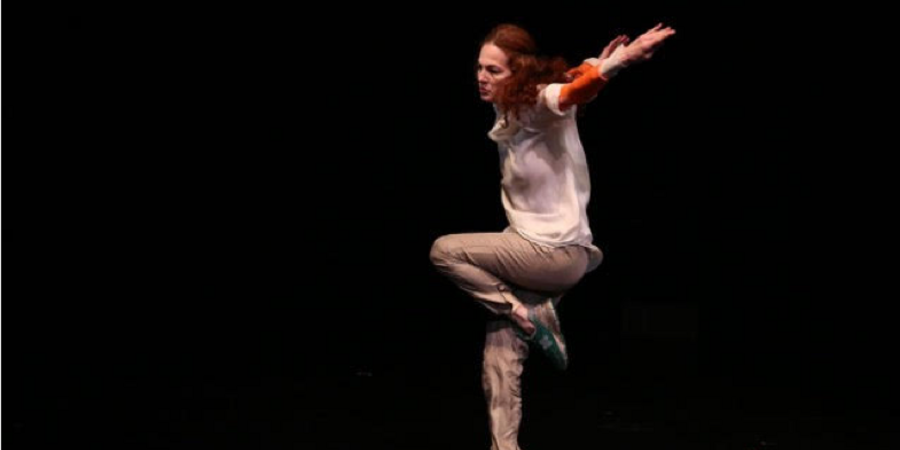 Woman with red hair dressed in white jumping in front of a black background