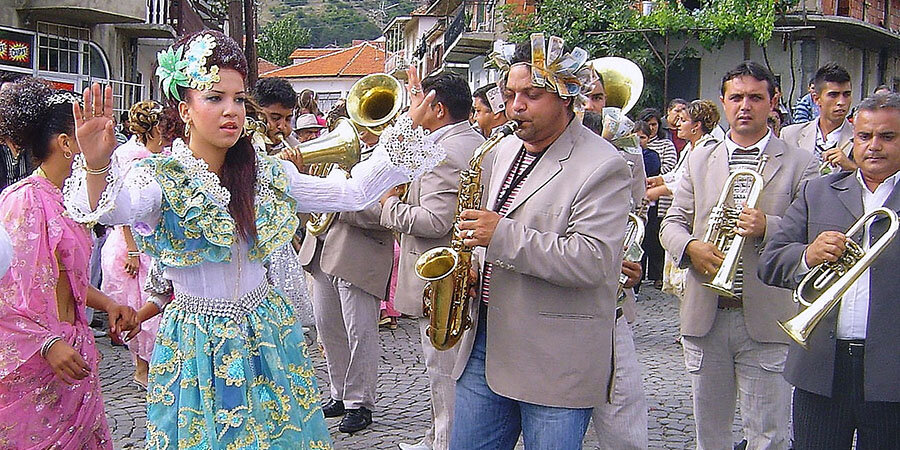 a brass band and ladies in colourful dresses in a street for a wedding celebration