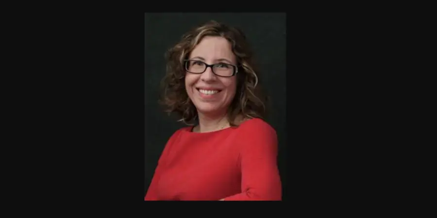 A woman (Stiliana Milkova) with dark hair wearing glasses smiles