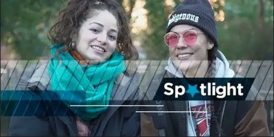 two people wearing hats and scarves as if for skiing, in front of trees