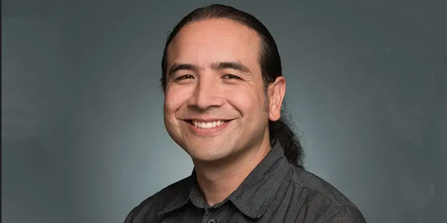 Smiling man in grey shirt with pony tail on smooth grey background