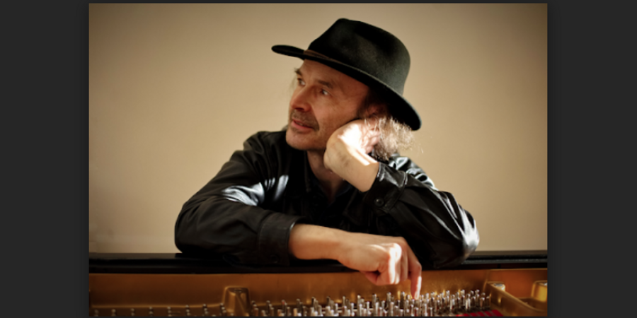 man in a hat leans over an open piano