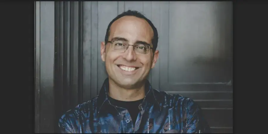 smiling man in blue shirt in front of a grey door