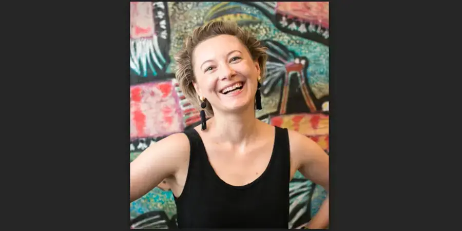smiling woman in black tank top in front of very colourful backdrop