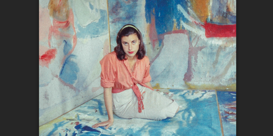 Helen Frankenthaler sitting in front of colourful canvas