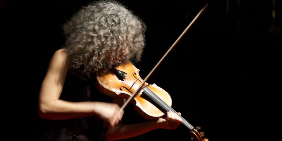 Woman with grey hair in profile playing violin in black background