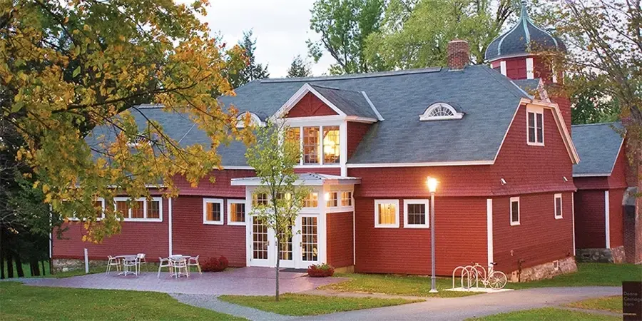 A red barn with a tree in the front, a table and chairs, and lights around the perimeter