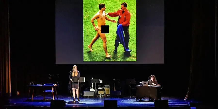 Live recording of Criminal Podcast. Woman with microphone on stage in front of a projection.