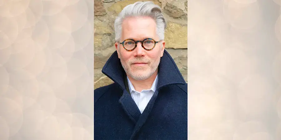 man with white hair and glasses wearing a black coat. 