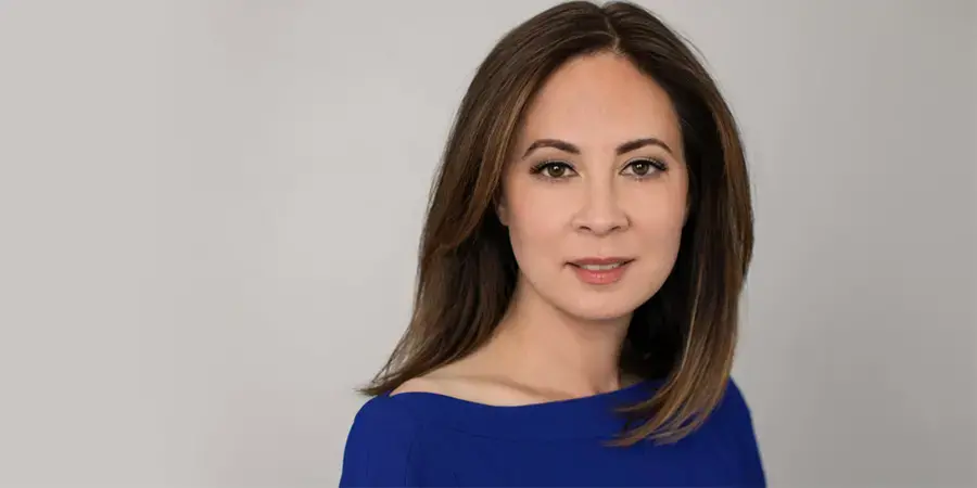 Paisley Rekdal, with dark smooth hair and a blue dress, stares at the camera 