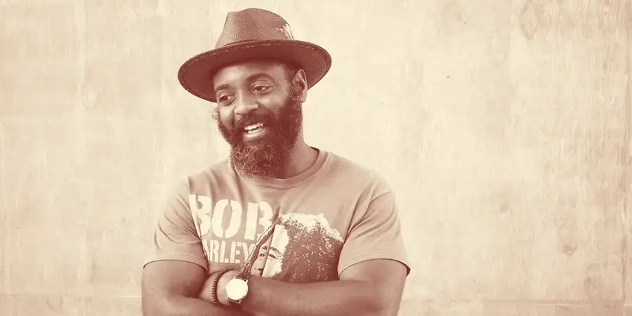 Reginald Dwayne Betts stands with arms crossed wearing a hat