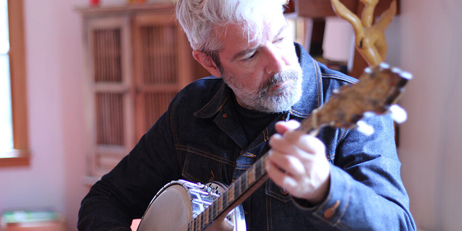 An older white man with a short grey beard playing banjo