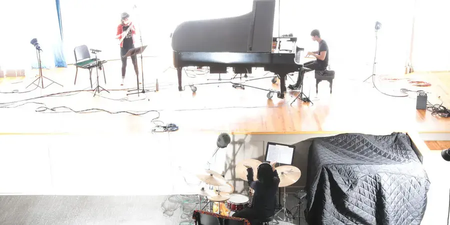 faded photo of a trio, piano, flute, drum set, in bright sunlight on a stage