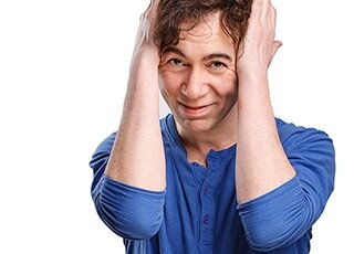 man with brown hair wearing a blue shirt and holding his head with his hands