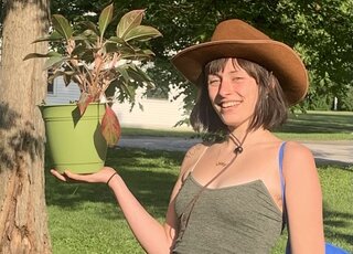 Photo of Jack de Loos; woman in green tank top, brown cowboy hat, holding plant