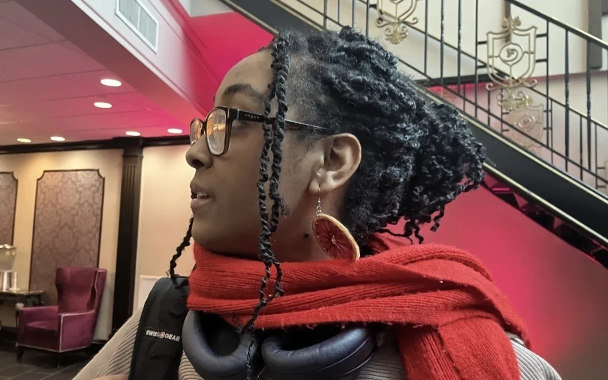 Blu Mehari '26 in right-facing profile wearing headphones and a red scarf around her neck and carrying a bag on her right shoulder