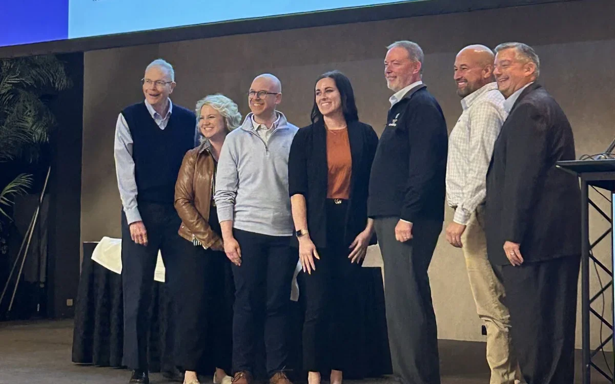 A group of seven smiling people on a stage