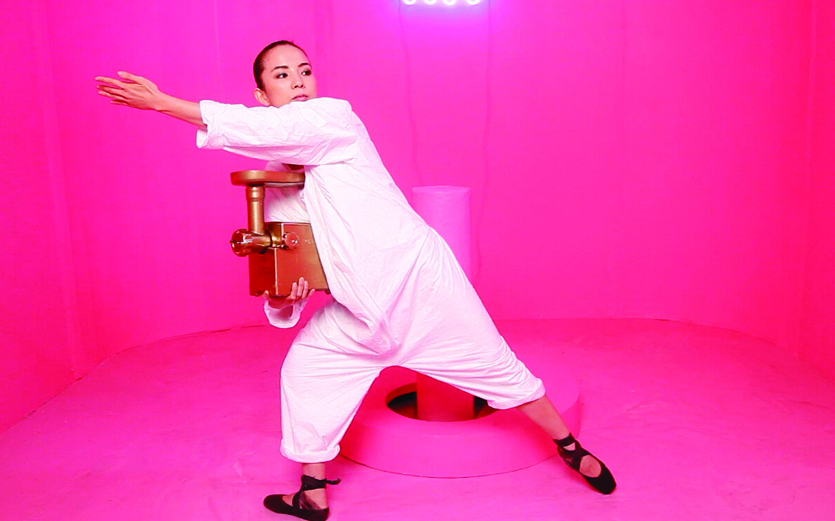 Jen Liu, wearing white, poses with arm extended in a bright pink/magenta painted room