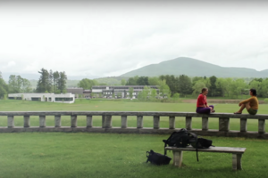 two students sitting on wall in front of expansive green misty campus and hills