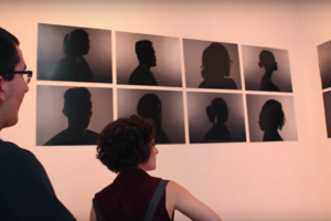 two humans in profile examine images of human profiles on a white wall