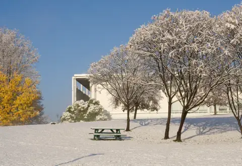 Snowy landscape with trees. picnic table, and campus building at Bennington College