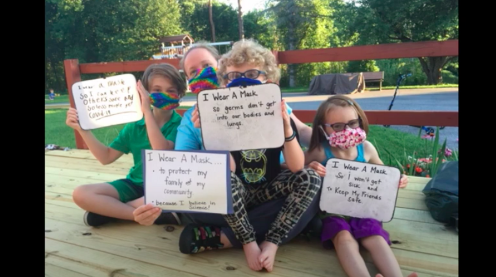 Image of family wearing masks and holding signs
