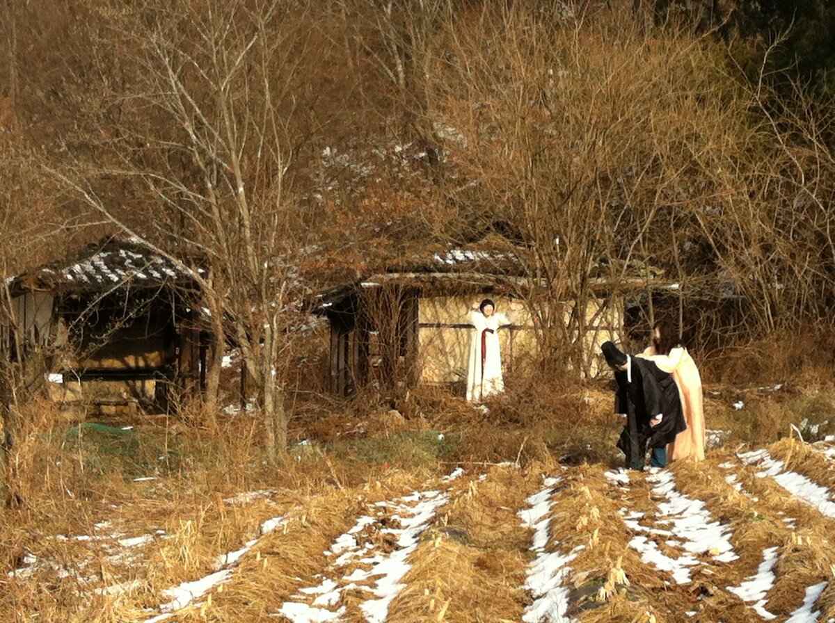 Three people play in the icy field in front of the traditional Korean house