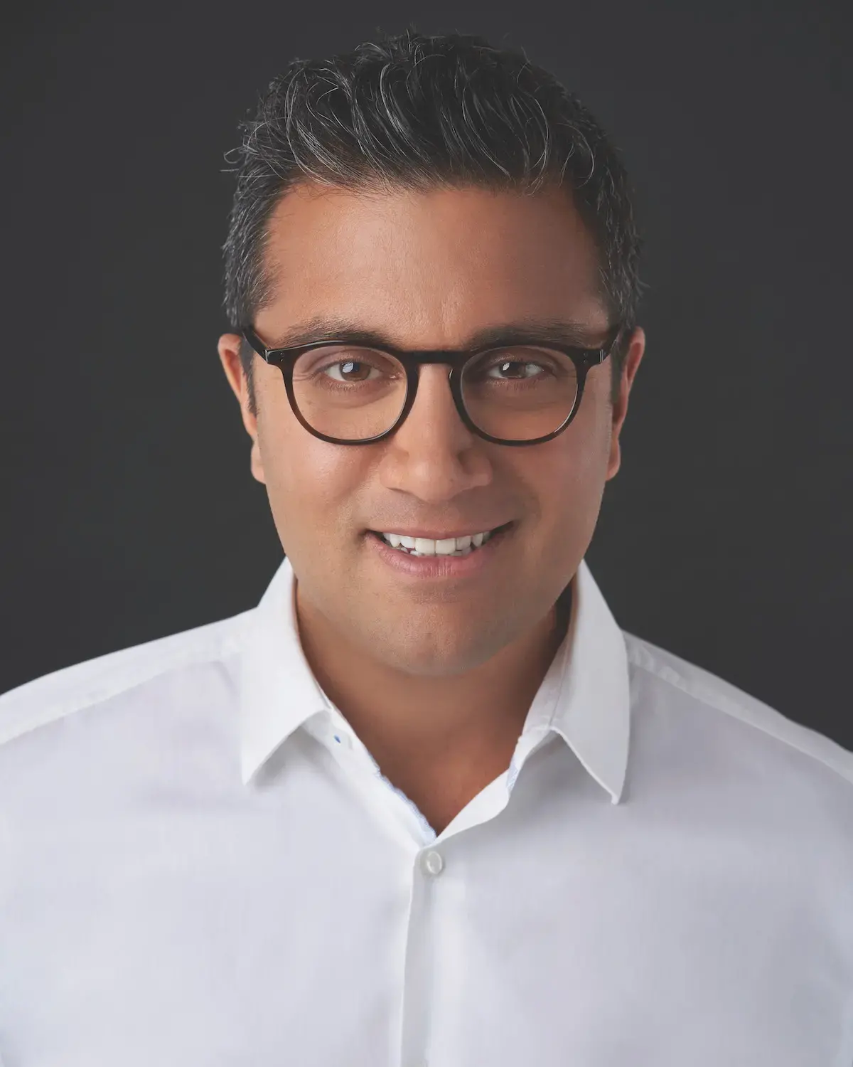Asad Ayaz white shirt and glasses with a dark background 
