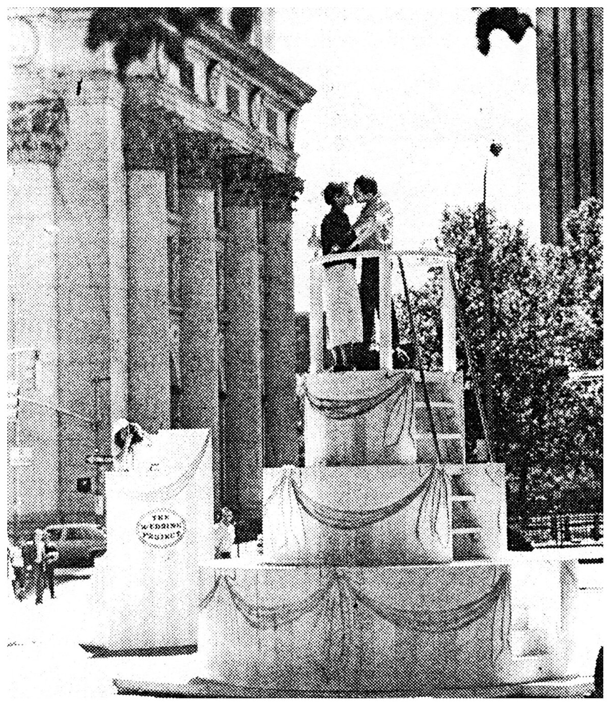 couple kissing on a giant wedding cake outside of city hall in black and white