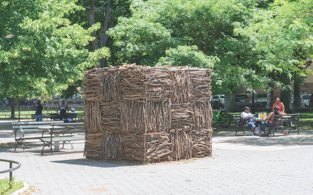 a huge hay cube with a checkerboard pattern in a park with trees