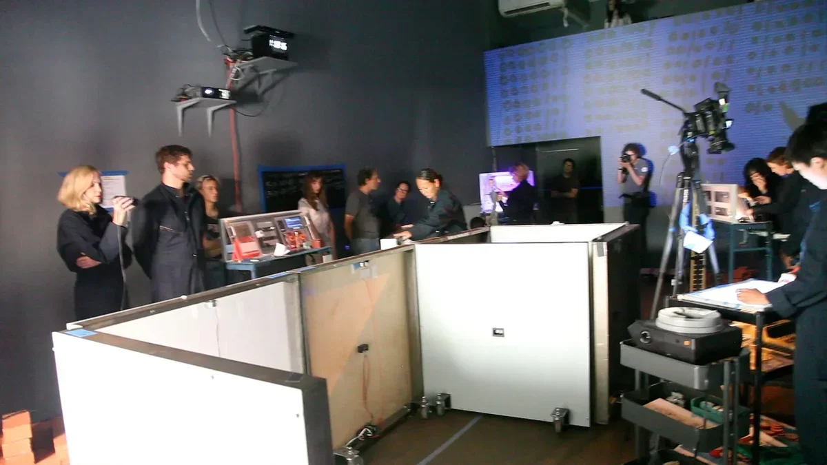 A performance installation where people move white, wheeled half-sized walls