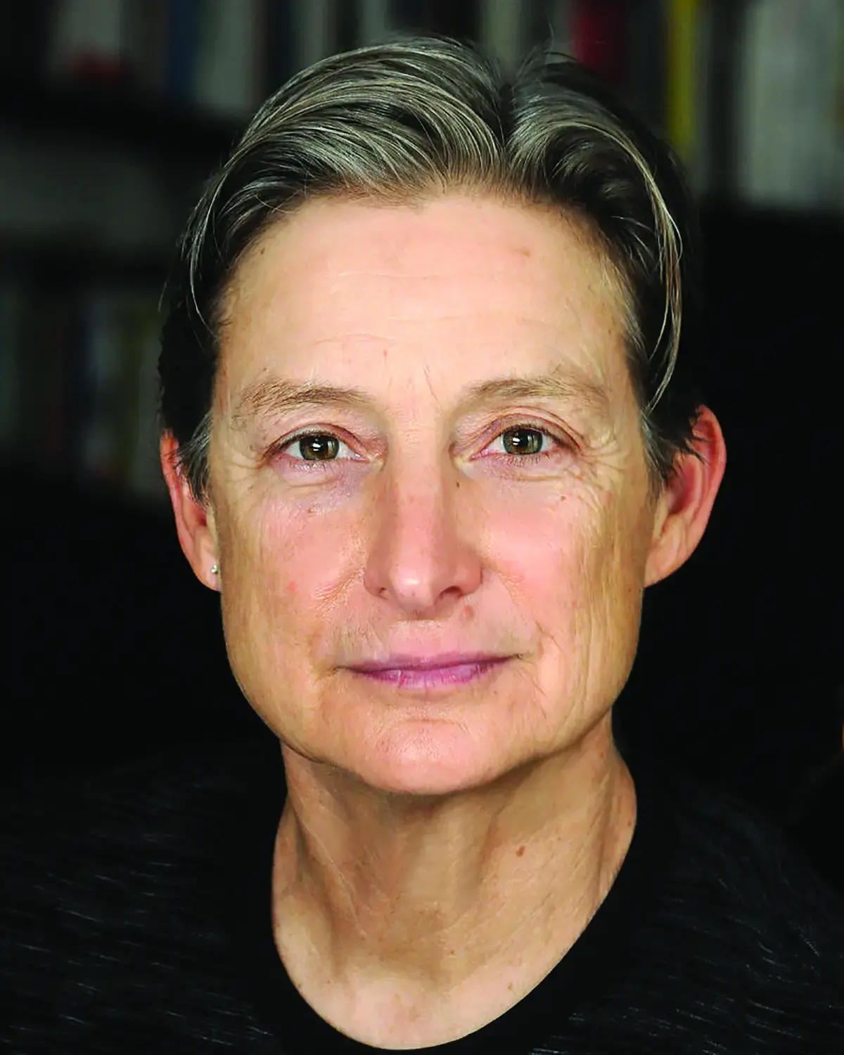 Woman with short grey hair and black shirt stares directly at camera