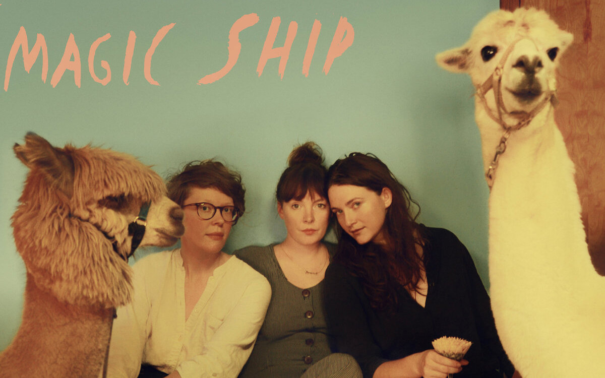 The three women of Mountain man sitting with two llamas for the Magic Ship album cover