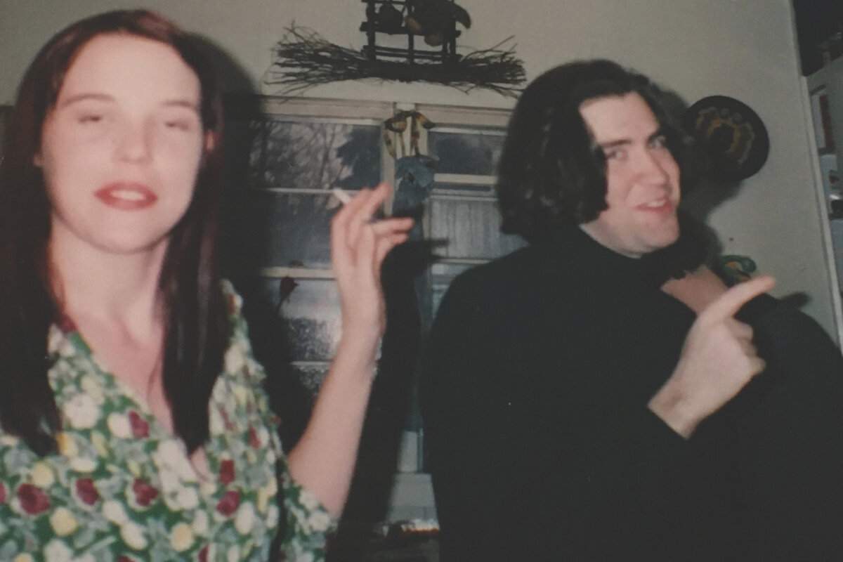 two students - a man and a woman - smile and smoke while at a party