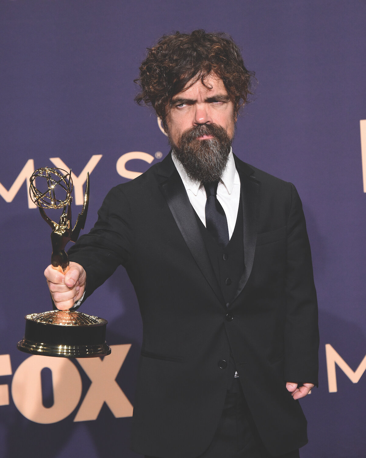 man with brown hair and beard holds emmy on the red carpet, purple background