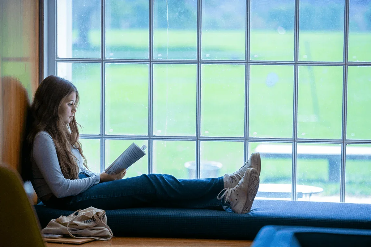 a student sits on a window seat while engrossed in a book