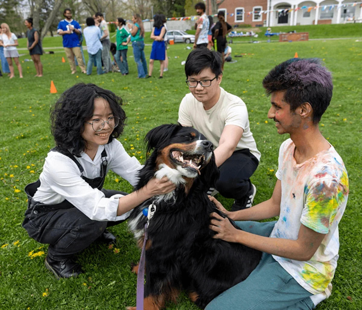 three students play with a visiting dog on the Lawn