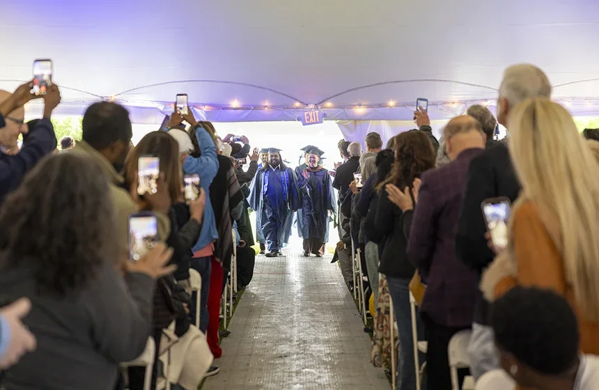 Two students lead the procession into the tent. The aisle is crowded with excited family and friends.