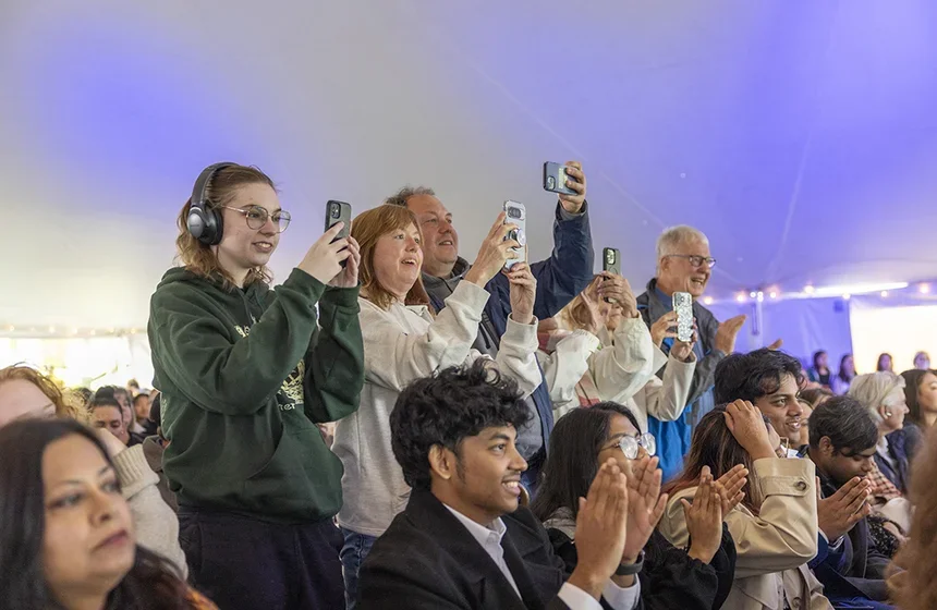 A row of excited family members record their student getting their diploma on their phones