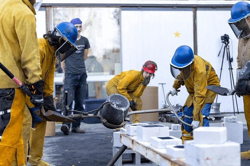 a group of students pour molten metal carefully wearing safety equipment