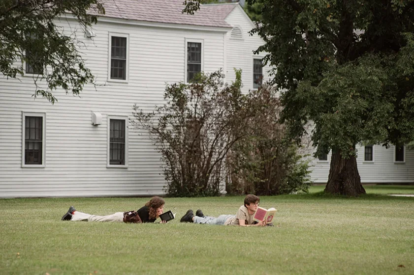 two students lie on the grass reading books