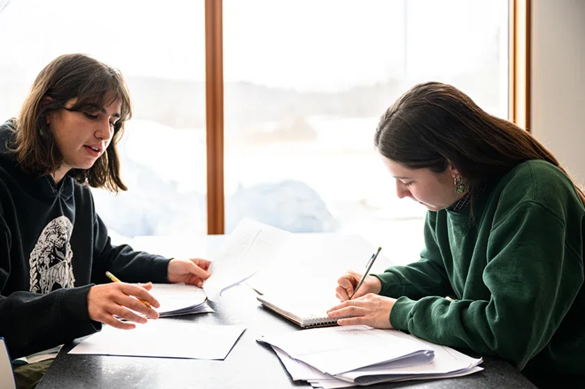 to students collaborate with writing at a table next to a window